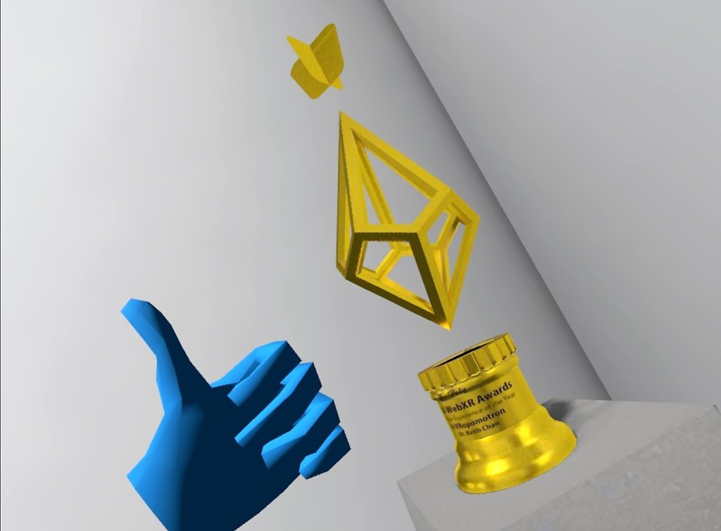 Gold model of the hovering WebXR trophy on a gray pedestal, with a thumbs-up hand next to it